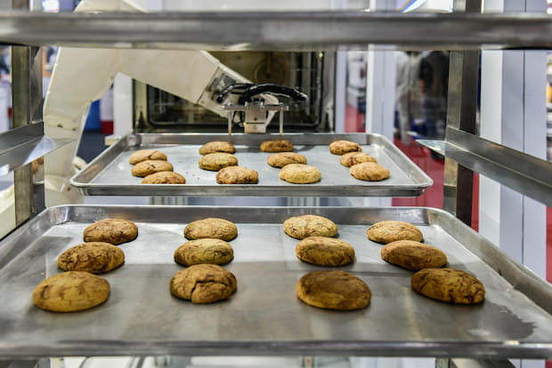 Robot arm preparing cookies for the oven in production line factory